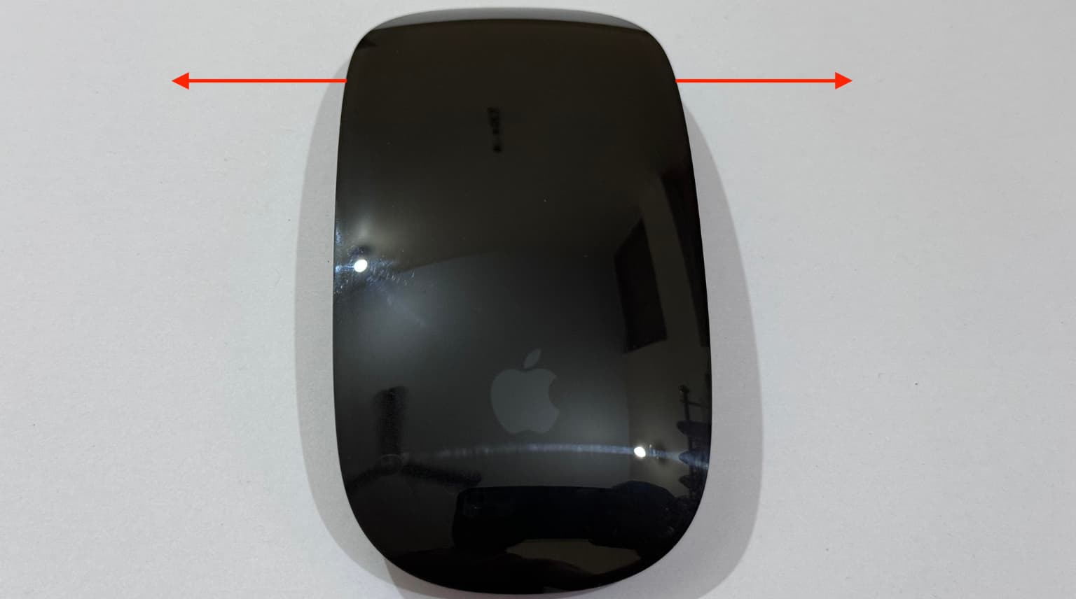 Apple Magic Mouse with two arrows showing that its top part moves left right very slightly